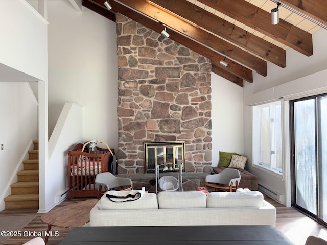 living room featuring beamed ceiling, wood-type flooring, high vaulted ceiling, baseboard heating, and a stone fireplace