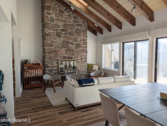 living room featuring dark wood-type flooring, high vaulted ceiling, beamed ceiling, and a stone fireplace