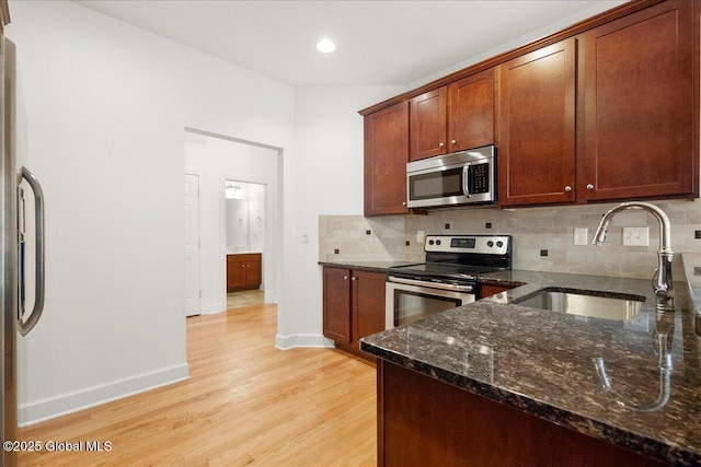 kitchen with sink, backsplash, dark stone counters, stainless steel appliances, and light hardwood / wood-style flooring