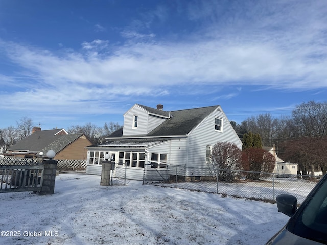 snow covered back of property featuring a sunroom