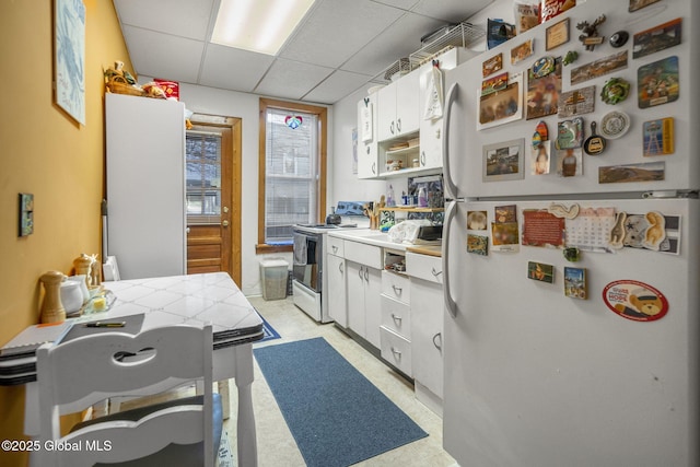 kitchen with white cabinetry, a drop ceiling, and white appliances