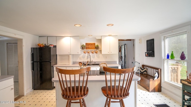 kitchen featuring sink, black refrigerator, white cabinets, and a breakfast bar area