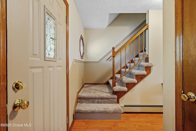 entryway with light wood-type flooring, a textured ceiling, and baseboard heating