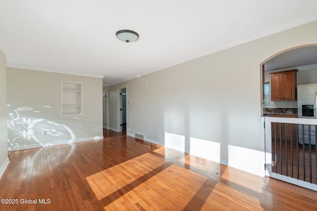 empty room with hardwood / wood-style flooring, built in shelves, and ornamental molding