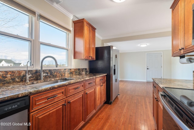 kitchen featuring appliances with stainless steel finishes, dark stone counters, crown molding, sink, and light hardwood / wood-style flooring