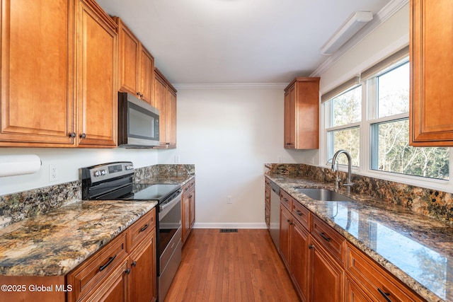 kitchen featuring sink, stainless steel appliances, light hardwood / wood-style flooring, dark stone counters, and ornamental molding