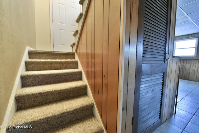 stairs with wood walls and tile patterned flooring