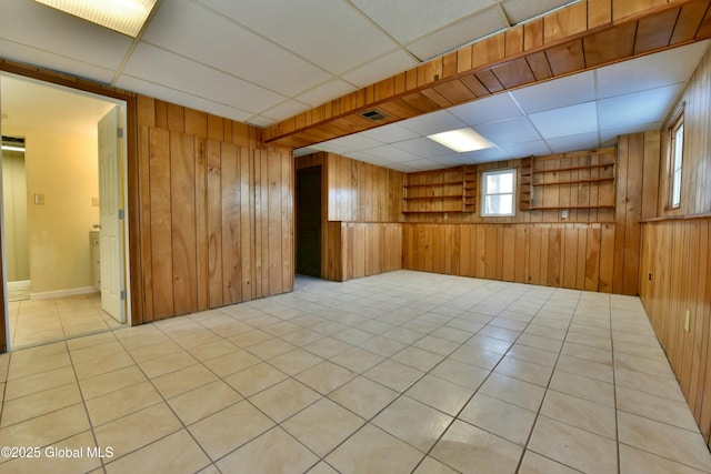 tiled empty room featuring a paneled ceiling and wooden walls