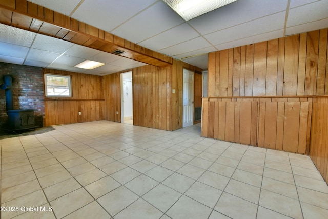 basement with a drop ceiling, wooden walls, and a wood stove