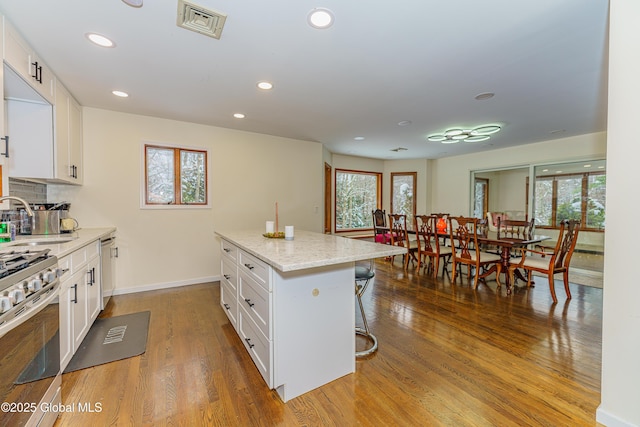 kitchen with a center island, wood-type flooring, light stone countertops, a kitchen bar, and white cabinetry