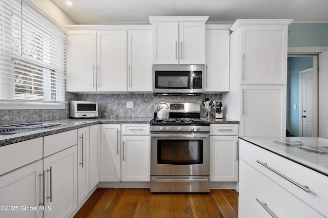 kitchen featuring backsplash, dark stone countertops, wood-type flooring, stainless steel appliances, and white cabinets