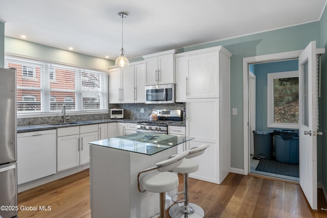 kitchen featuring backsplash, hardwood / wood-style flooring, hanging light fixtures, appliances with stainless steel finishes, and white cabinets