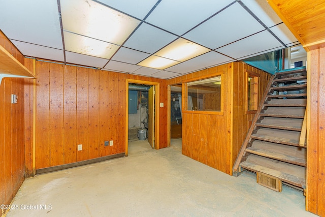 basement featuring a paneled ceiling, wooden walls, and electric panel