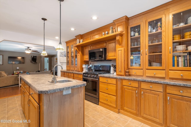 kitchen with ceiling fan, pendant lighting, a center island with sink, sink, and stainless steel gas range