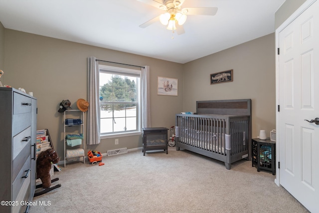 bedroom with ceiling fan, light colored carpet, and a crib