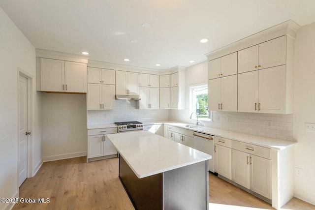 kitchen featuring appliances with stainless steel finishes, light wood-type flooring, sink, a center island, and white cabinetry