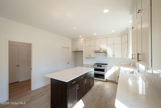 kitchen featuring a center island, white cabinets, stainless steel range with gas cooktop, sink, and light hardwood / wood-style floors