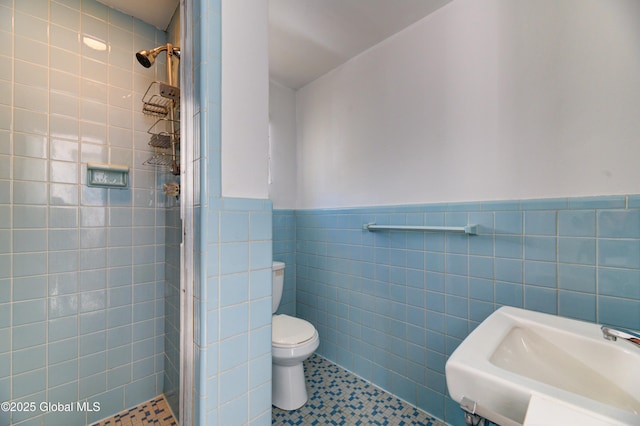 bathroom with tile patterned floors, sink, toilet, tiled shower, and tile walls