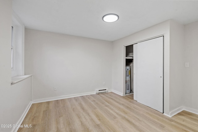 unfurnished bedroom featuring baseboard heating, electric water heater, a closet, and light hardwood / wood-style floors