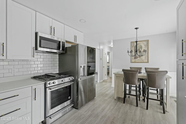 kitchen with decorative light fixtures, a breakfast bar, an inviting chandelier, appliances with stainless steel finishes, and white cabinets