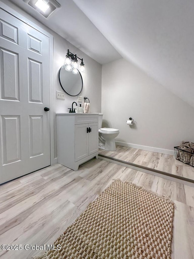 bathroom featuring lofted ceiling, toilet, vanity, and wood-type flooring