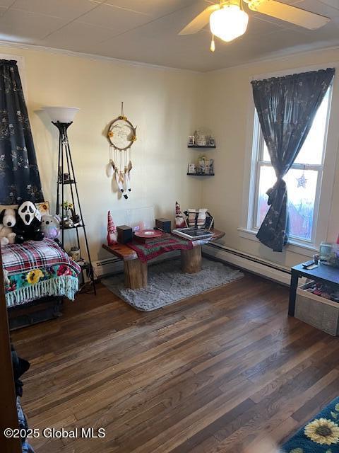 living area featuring dark hardwood / wood-style floors, baseboard heating, ornamental molding, and ceiling fan