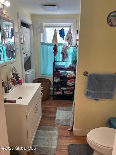 bathroom with stacked washer / dryer, toilet, vanity, and hardwood / wood-style flooring