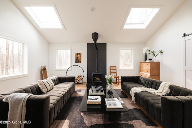 living room with a barn door, lofted ceiling with skylight, a wood stove, and plenty of natural light