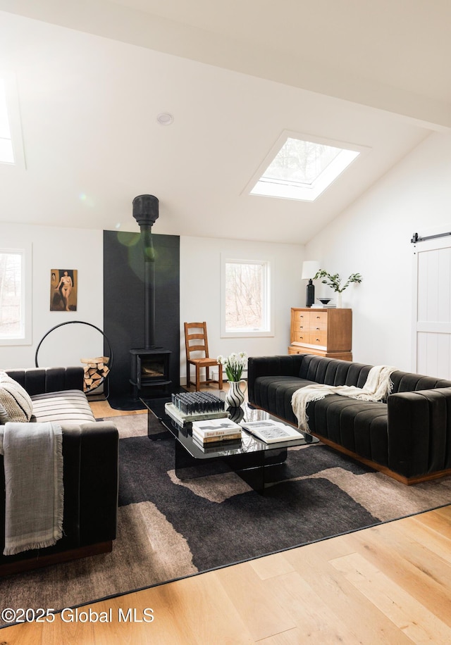 living room with hardwood / wood-style flooring, lofted ceiling with skylight, a wood stove, and plenty of natural light