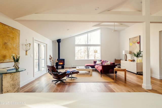 living area featuring light hardwood / wood-style floors, lofted ceiling with beams, and a wood stove