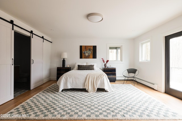 bedroom featuring a baseboard heating unit, a barn door, and hardwood / wood-style flooring