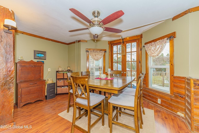 dining room featuring french doors, ceiling fan, light hardwood / wood-style flooring, and wooden walls