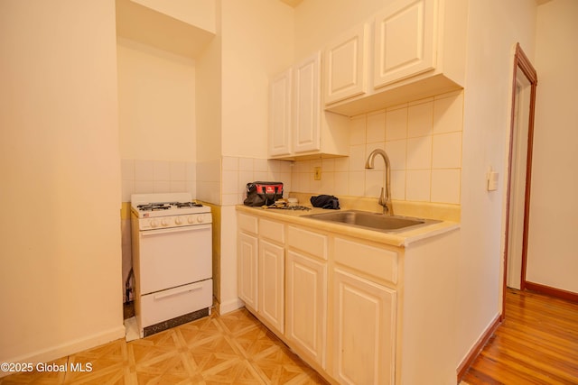 kitchen featuring sink, decorative backsplash, white gas range oven, and white cabinetry