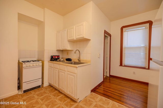 kitchen featuring white cabinets, light parquet floors, white gas range oven, sink, and tasteful backsplash