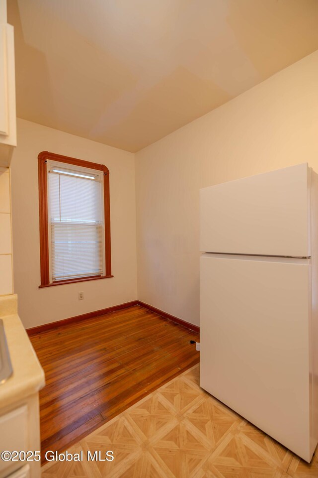 kitchen featuring light parquet flooring, white refrigerator, and white cabinetry