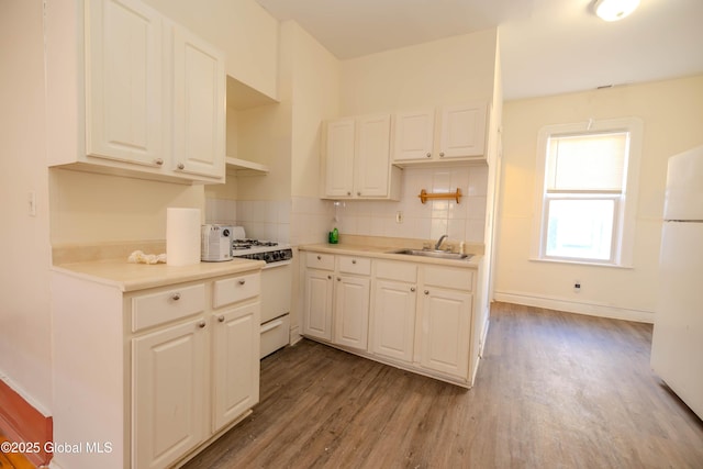 kitchen with white appliances, tasteful backsplash, light wood-type flooring, white cabinets, and sink