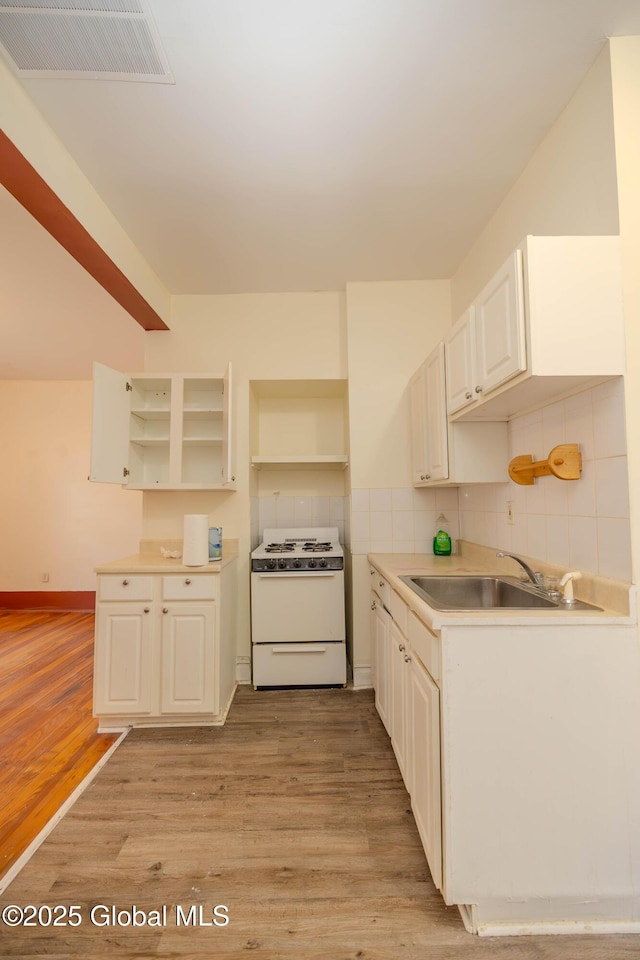 kitchen featuring white stove, light hardwood / wood-style floors, backsplash, and sink