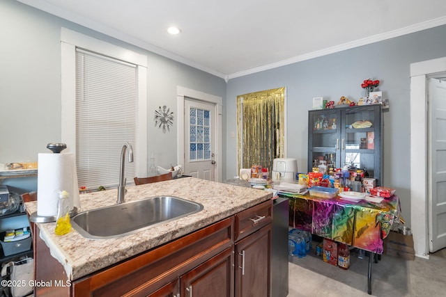 kitchen with crown molding, sink, a center island with sink, and light stone counters