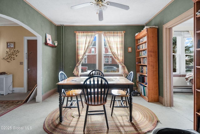 carpeted dining space with a baseboard heating unit, ceiling fan, a wealth of natural light, and ornamental molding