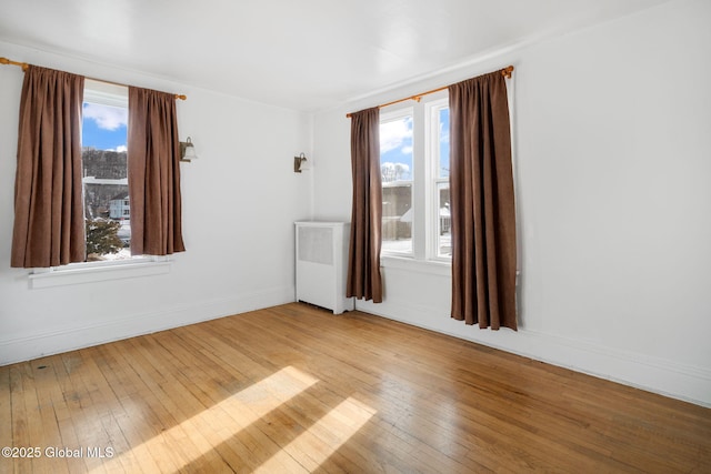 unfurnished room with radiator, a healthy amount of sunlight, and hardwood / wood-style floors