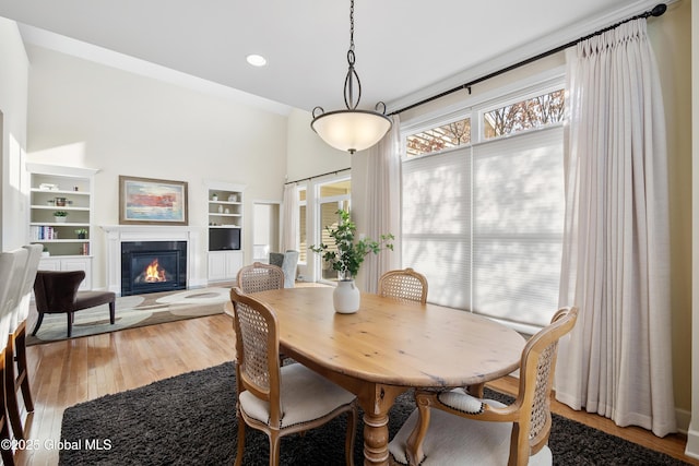 dining area featuring plenty of natural light, wood-type flooring, a tiled fireplace, and built in shelves