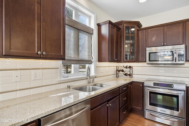 kitchen featuring light stone countertops, stainless steel appliances, light hardwood / wood-style floors, sink, and backsplash