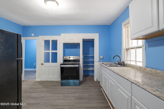 kitchen with black refrigerator, white cabinetry, electric range, and sink