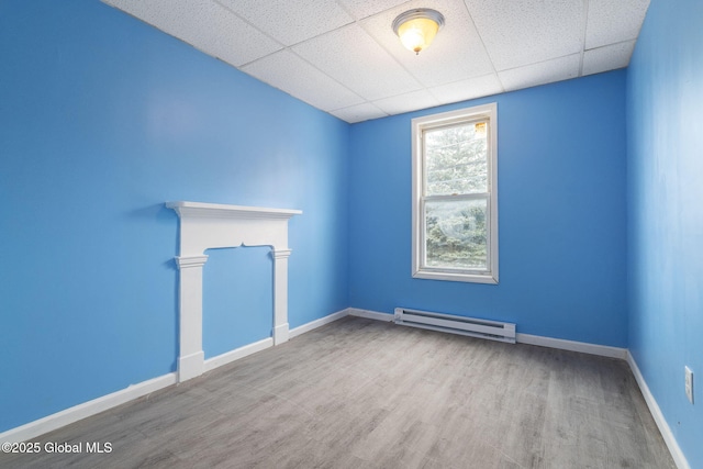 unfurnished room featuring a baseboard heating unit, a drop ceiling, and wood-type flooring