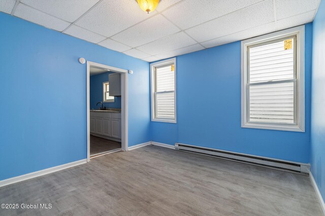 spare room with sink, hardwood / wood-style floors, a baseboard heating unit, and a drop ceiling