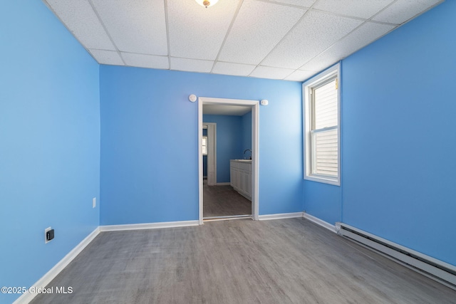 unfurnished room with a paneled ceiling, a baseboard heating unit, and hardwood / wood-style floors