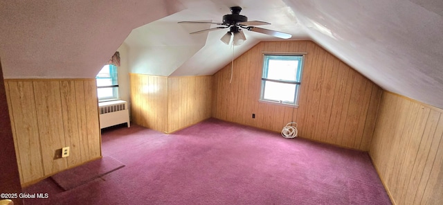 bonus room with vaulted ceiling, radiator heating unit, wooden walls, ceiling fan, and dark carpet