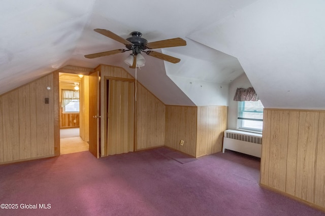 bonus room featuring wooden walls, radiator heating unit, ceiling fan, and vaulted ceiling