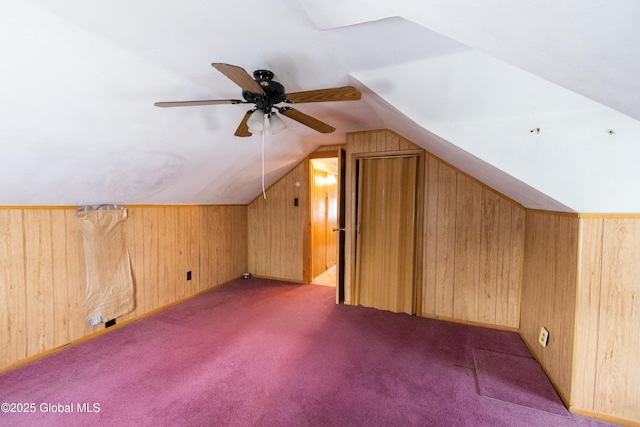 bonus room with vaulted ceiling, ceiling fan, wooden walls, and light carpet