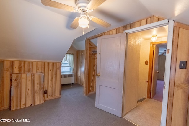 additional living space featuring wooden walls, vaulted ceiling, ceiling fan, radiator heating unit, and light colored carpet